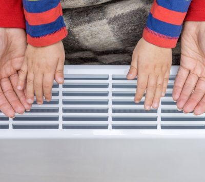 Une femme et un enfant ce réchauffent les mains sur un radiateur