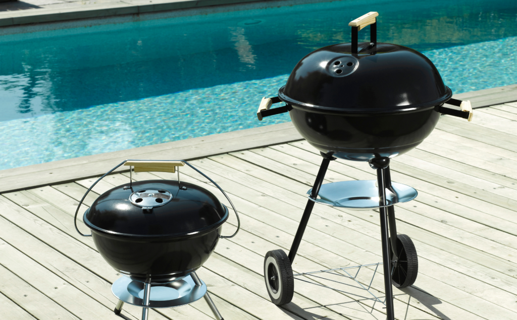 Barbecue ou plancha : zoom sur le barbecue au charbon. Deux barbecues boules devant une piscine et sur une terrasse en bois