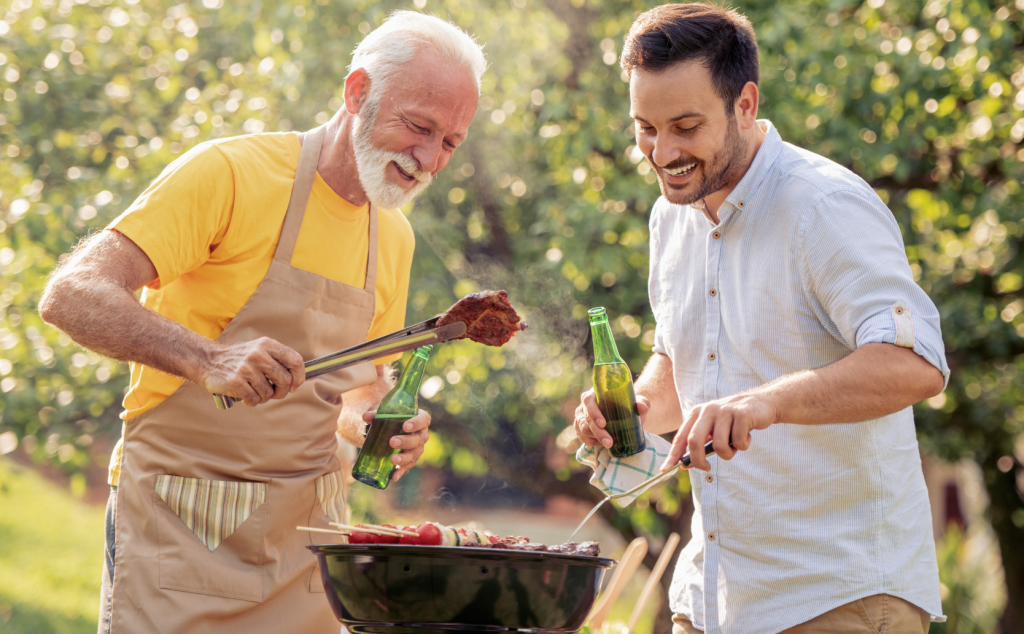 Objectif convivialité : deux hommes autour d'un barbecue ou plancha, avec une bouteille dans la mer et des brochettes à cuire